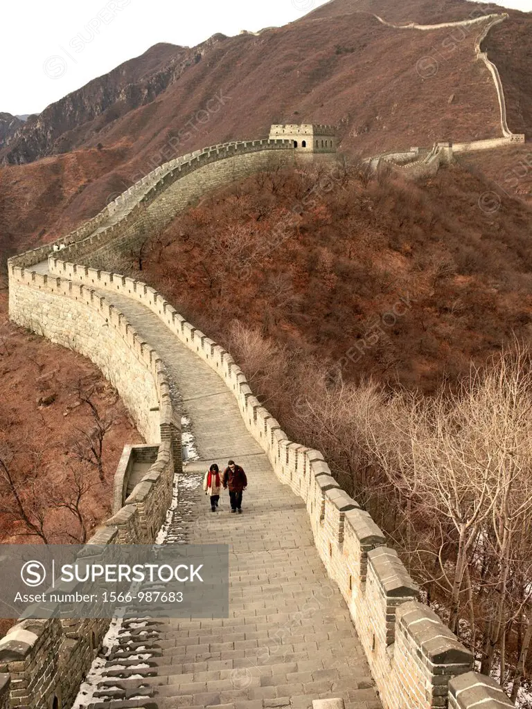A couple dressed in winter coats walks on a section of the Great Wall of China near Beijing, China