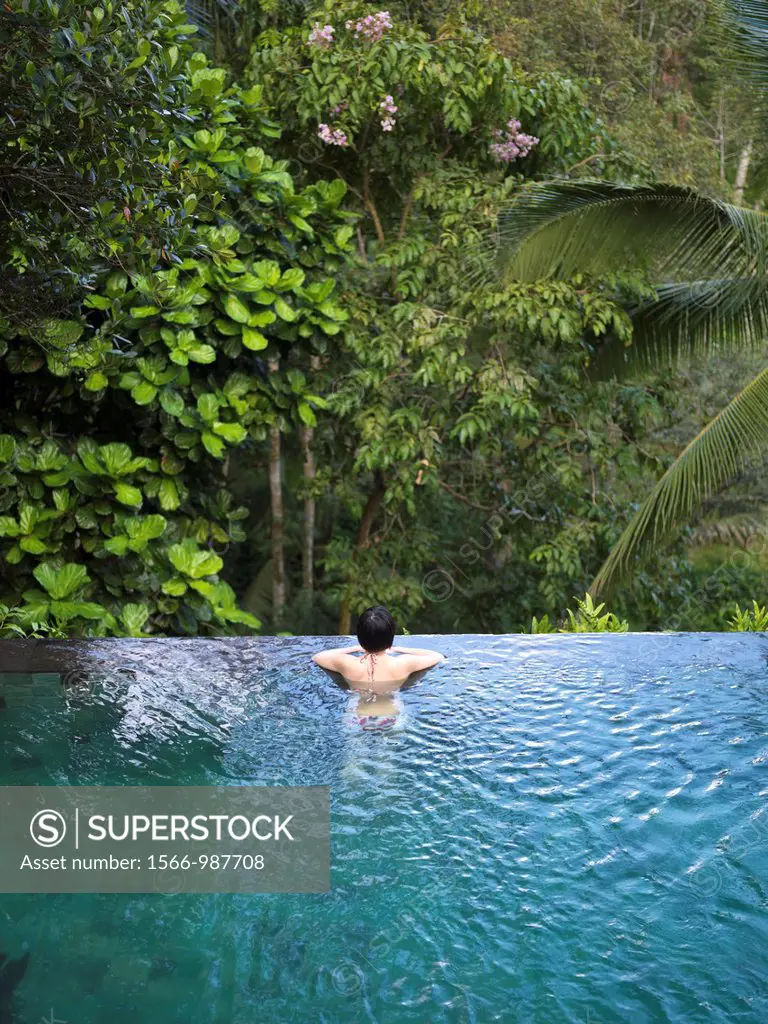 Woman bathing in an infinity pool surrounded by a lush tropical forest