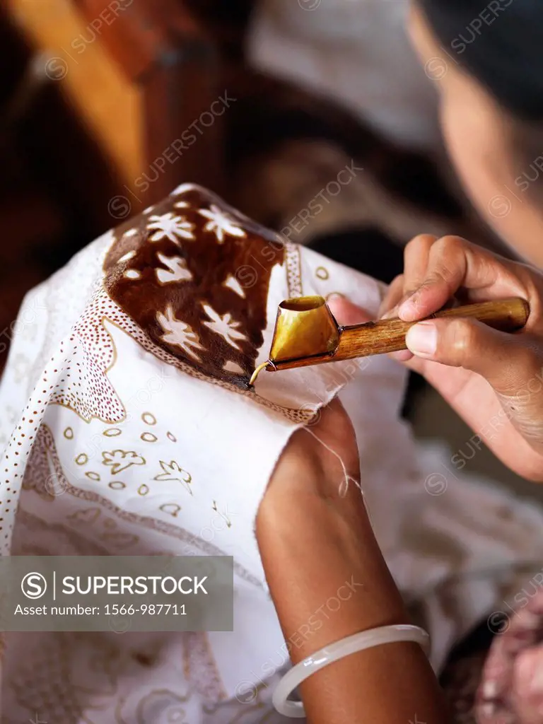 A woman applies liquid wax to a fabric with a canting, which is used in batik making Batik is a wax-resist dyeing technique used on textile
