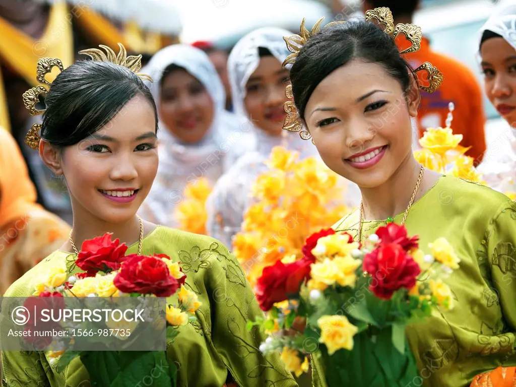 Two young Malaysian women holding bouquets of flowers dressed in formal traditional Malaysian dresses and headpieces