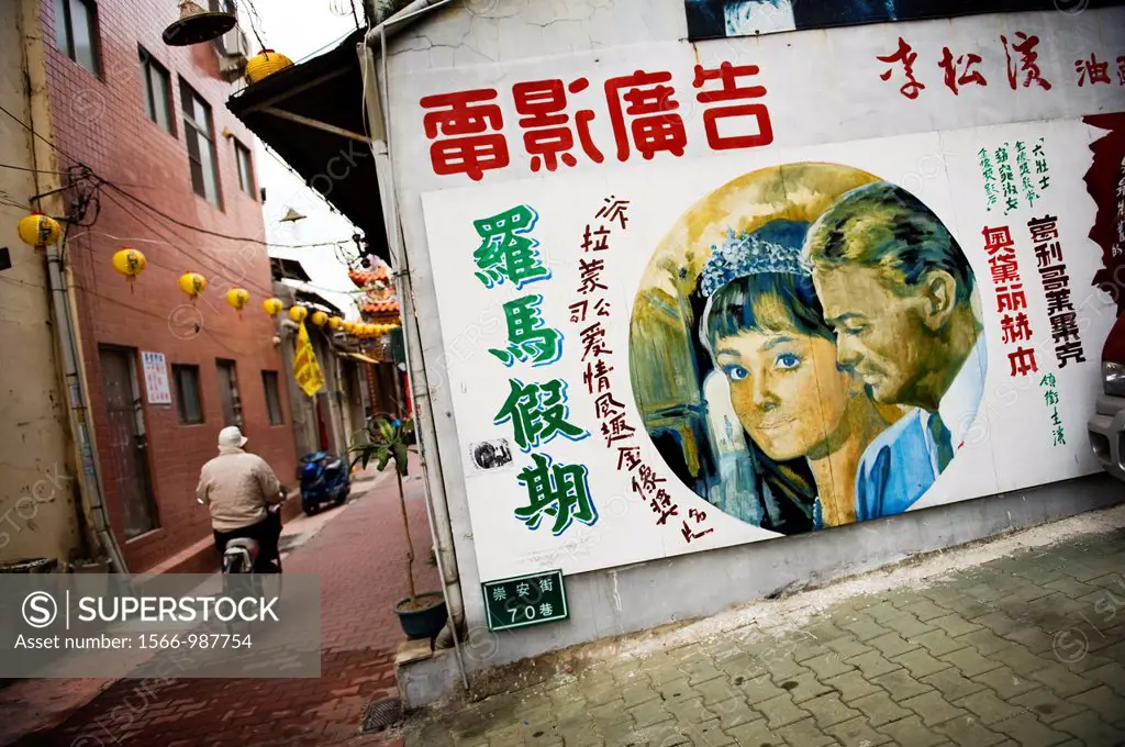 A man on a bicycle rides pass what appears to be an ad for an Audrey Hepburn movie in Taipei, Taiwan