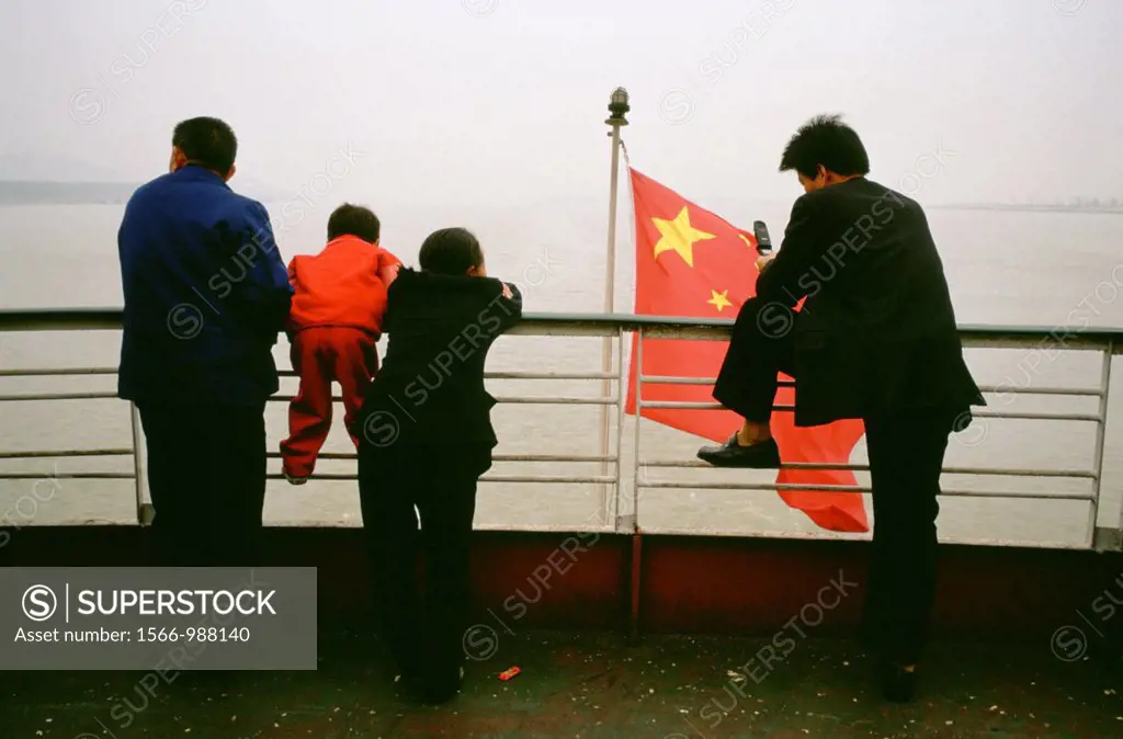 A businessman on the back of a ship sailing down the Yangtze River in China, with the Chinese national flag flying behind him, a peasant family leans ...
