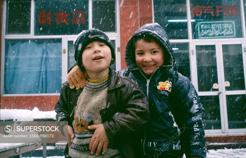 Two Chinese Uygur children play together outside in the snow