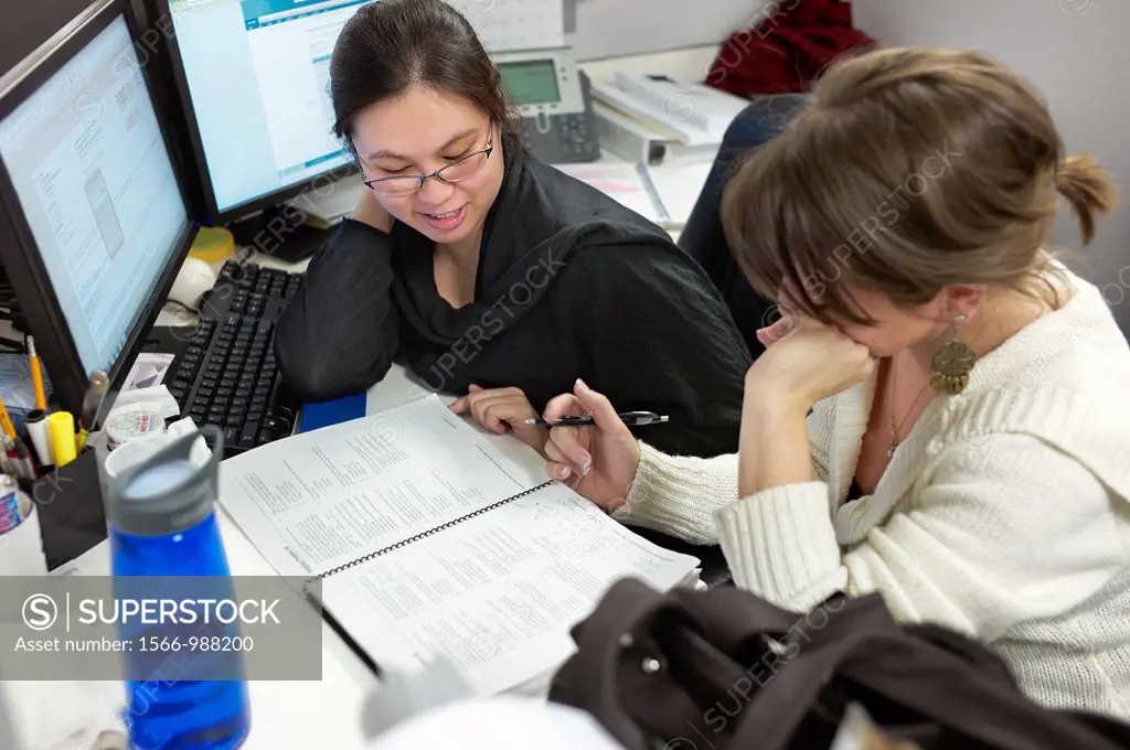 Two women checking paperwork in their cubicle