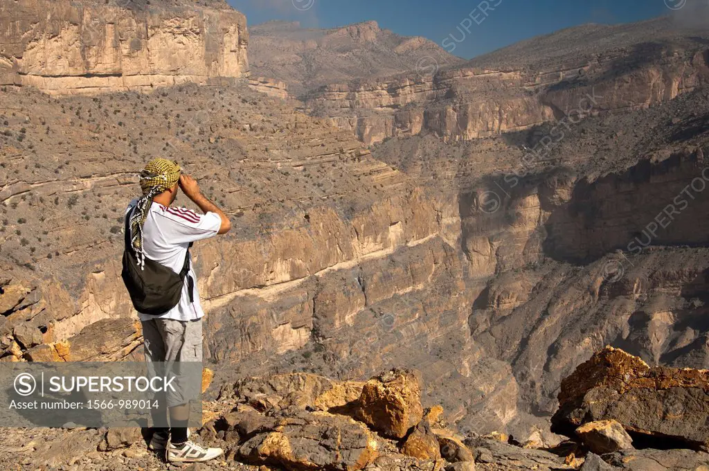 Omani hiker looking into a gorge in the Grand Canyon of Oman in Wadi Nakhur at the foot of Jebel Shams, Al Hajar Mountains, Sultanate of Oman