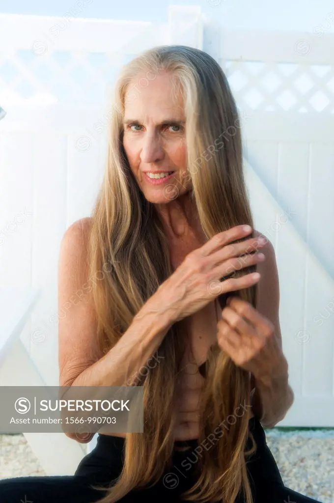 Partially nude 57 year old woman pulling on her long hair smiling at the camera