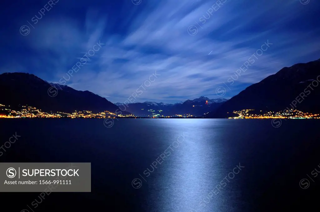 Reflected moon light over an alpine lake maggiore with snow-capped mountains and clouds in ticino switzerland