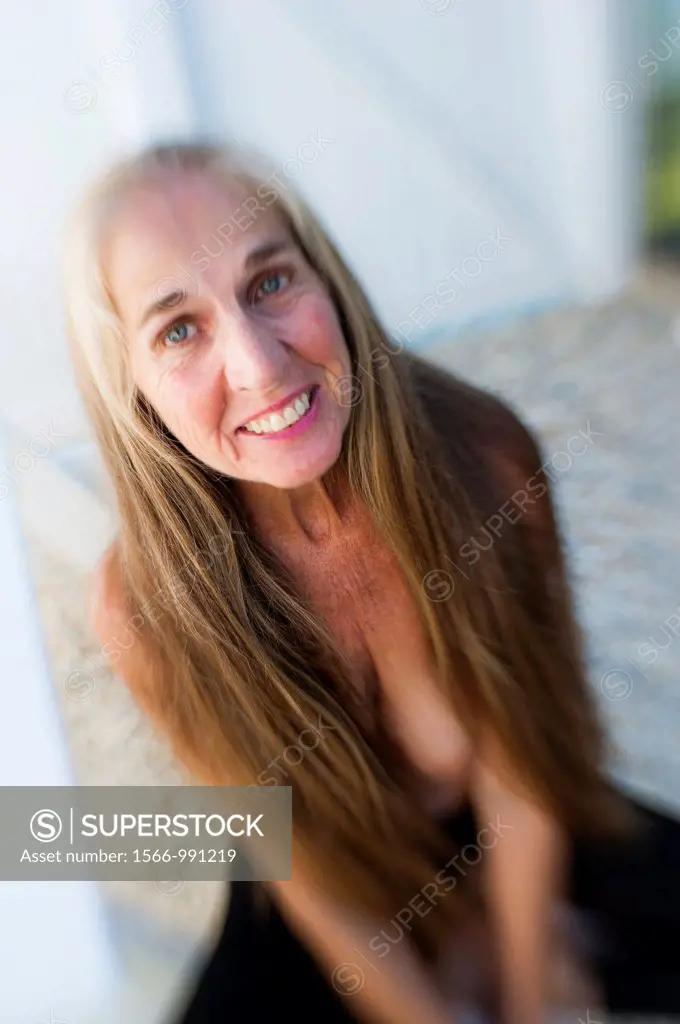 Partially nude 57 year old woman with long hair smiling up at the camera