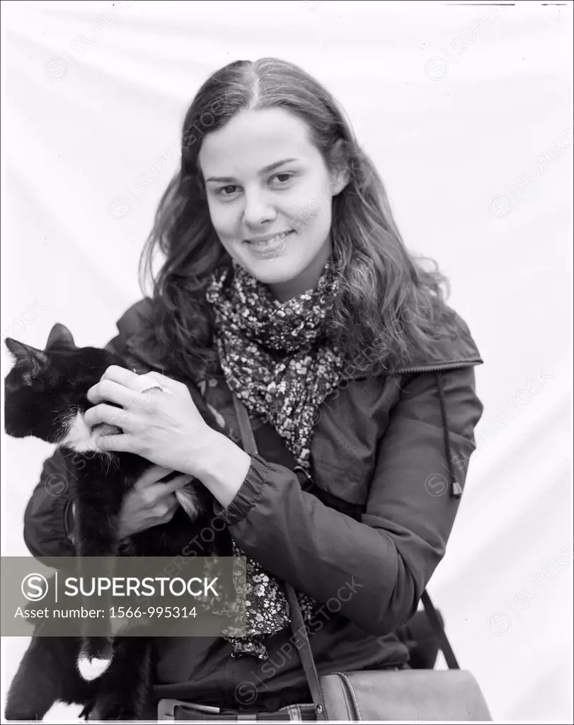 Rotterdam, Netherlands. Portrait of a young woman, petting her cat, against white sheet background. Analog Black & White film.