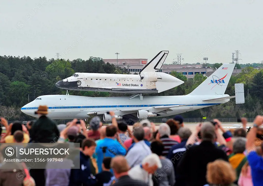 A crowd watch as the space shuttle Discovery, sitting on top of a modified Boeing 747 aircraft, taxis on the runway at Washington Dulles International...