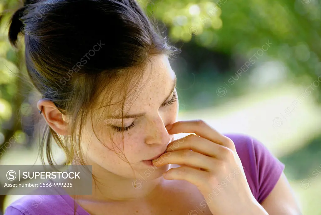 20 years old woman in a garden biting her finger nails