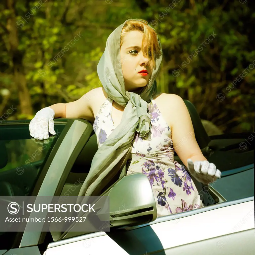 Woman wearing a headscarf stands next to a convertible