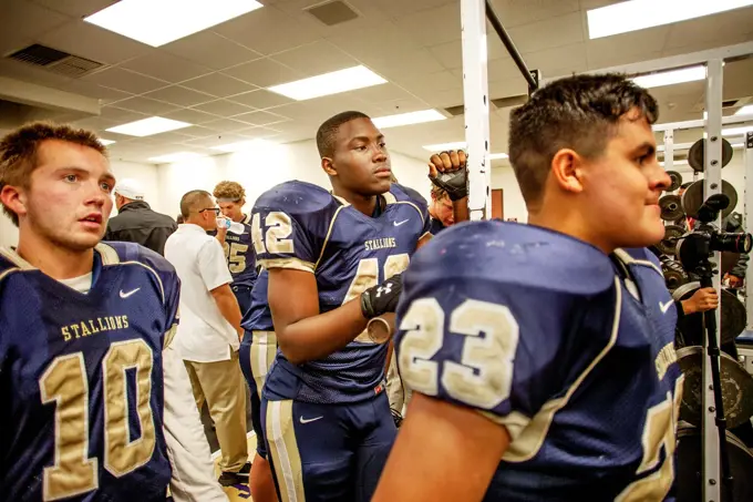 High school football players listen to their coach during half time of a night game in San Juan Capistrano, CA.