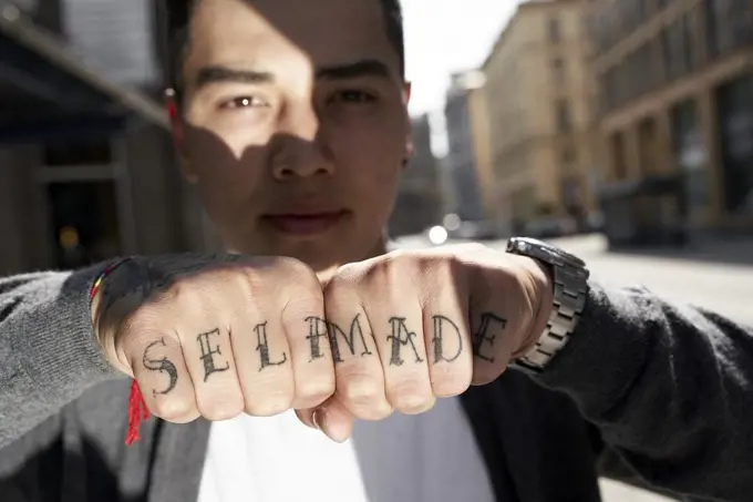 Young Asian man showing the message ""self made"" tattoed on his fingers