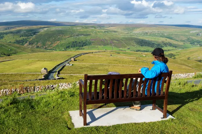 Female hiker on seat overlooking Buttertubs pass in The Yorkshire Dales National Park. Yorkshire, England, UK. View over Buttertubs pass, Swaledale an...