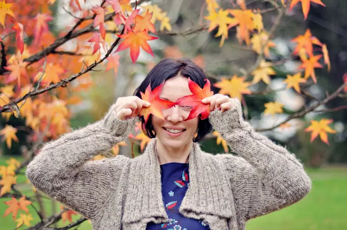 Smiling mid adult woman holding leaf close to her face, autumn