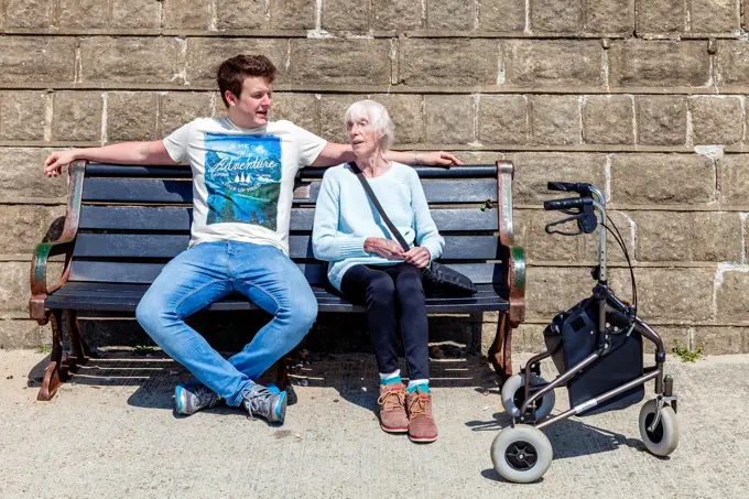 An Elderly Disabled Woman Sitting On A Bench Talking To Her Grandson, Brighton, Sussex, UK.