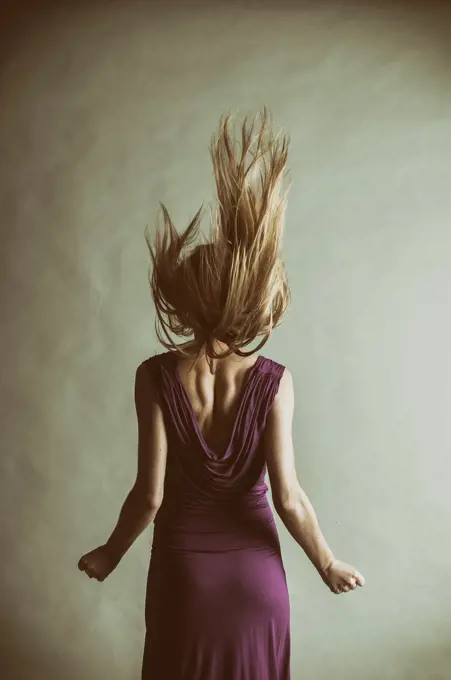 Rear view of a young blond woman wearing a purple dress flicking her hair up.