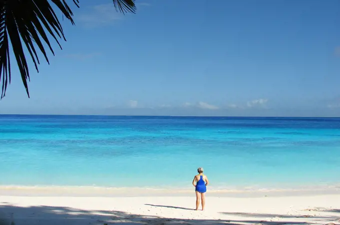 A blue-sky day at the beach in Mahe, the Seychelles. A woman in a blue bathing suit has the beach all to herself.