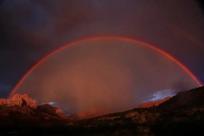 A full rainbow stretches across the sky during a lightning and thunderstorm at Zion National Park, Utah