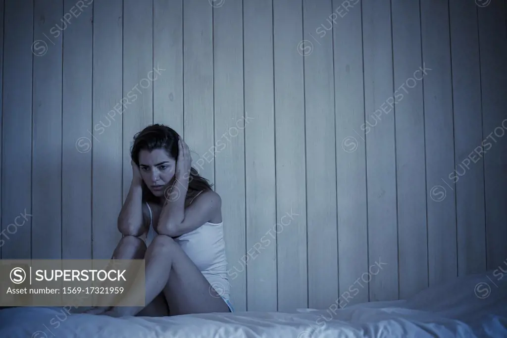 Sad young woman sitting on bed