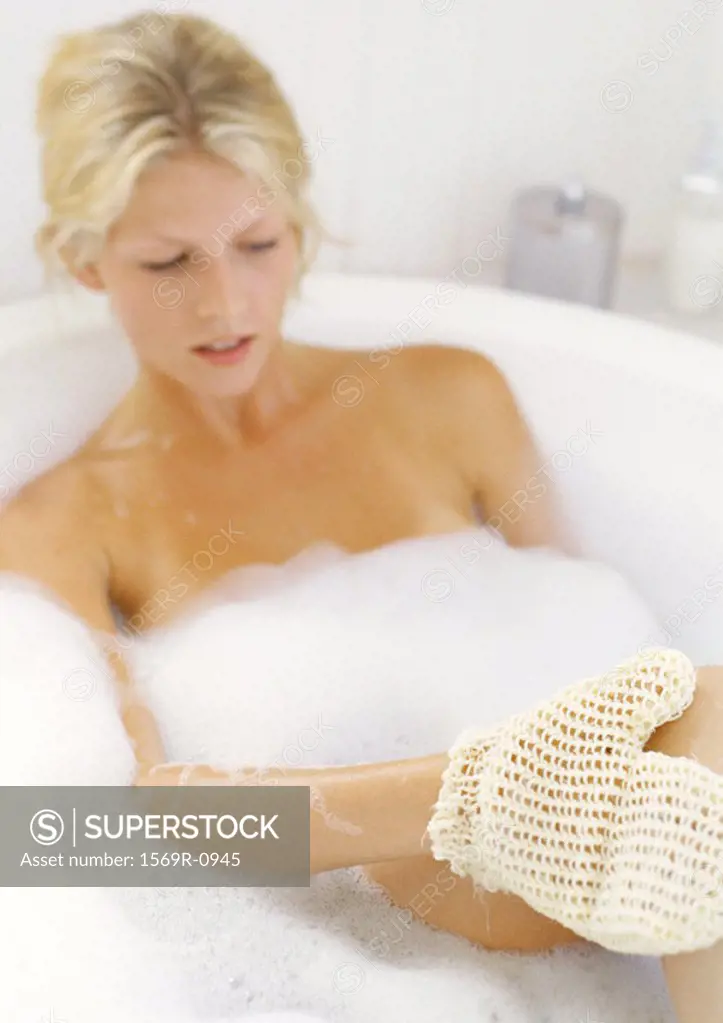 Young woman in bathtub using masage glove