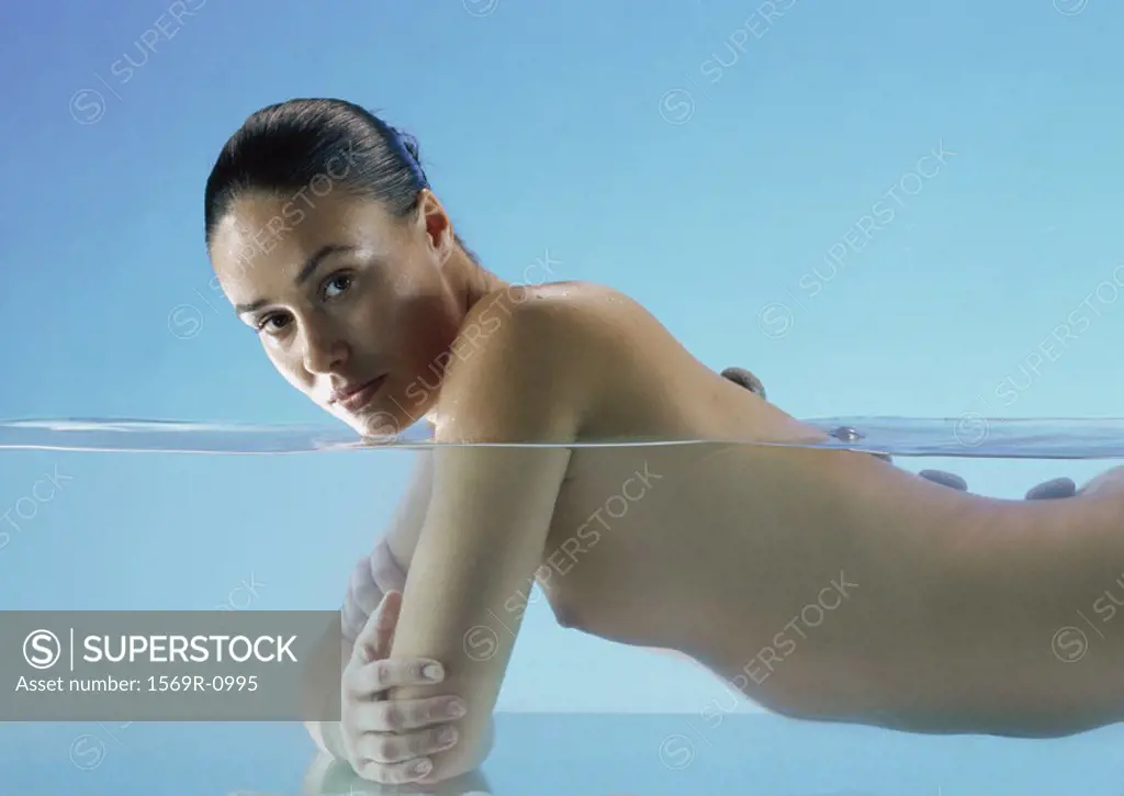 Nude woman doing lastone therapy in water, looking at camera