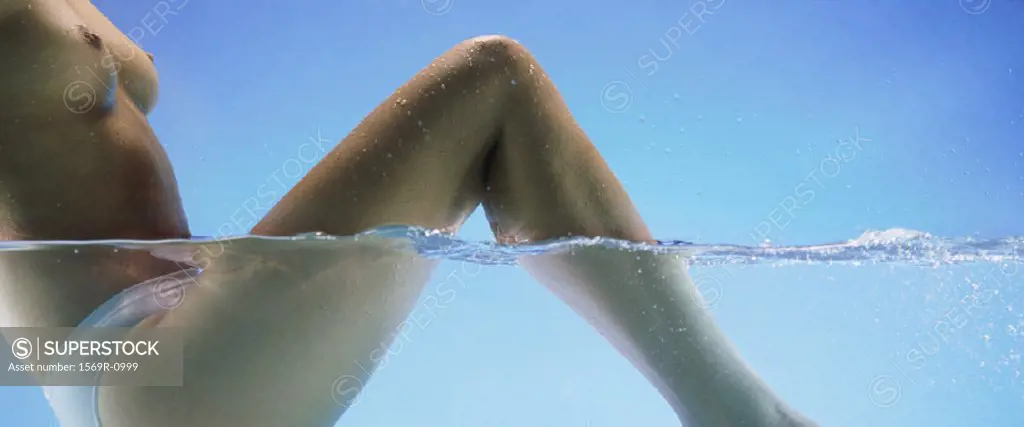 Semi-nude woman sitting in water with knees up, side view