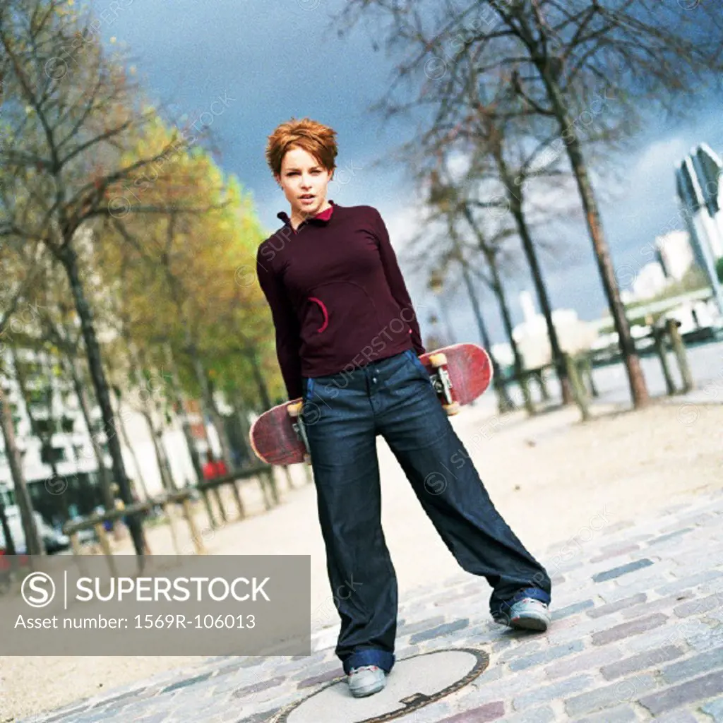 Young woman holding a skateboard behind her, portrait