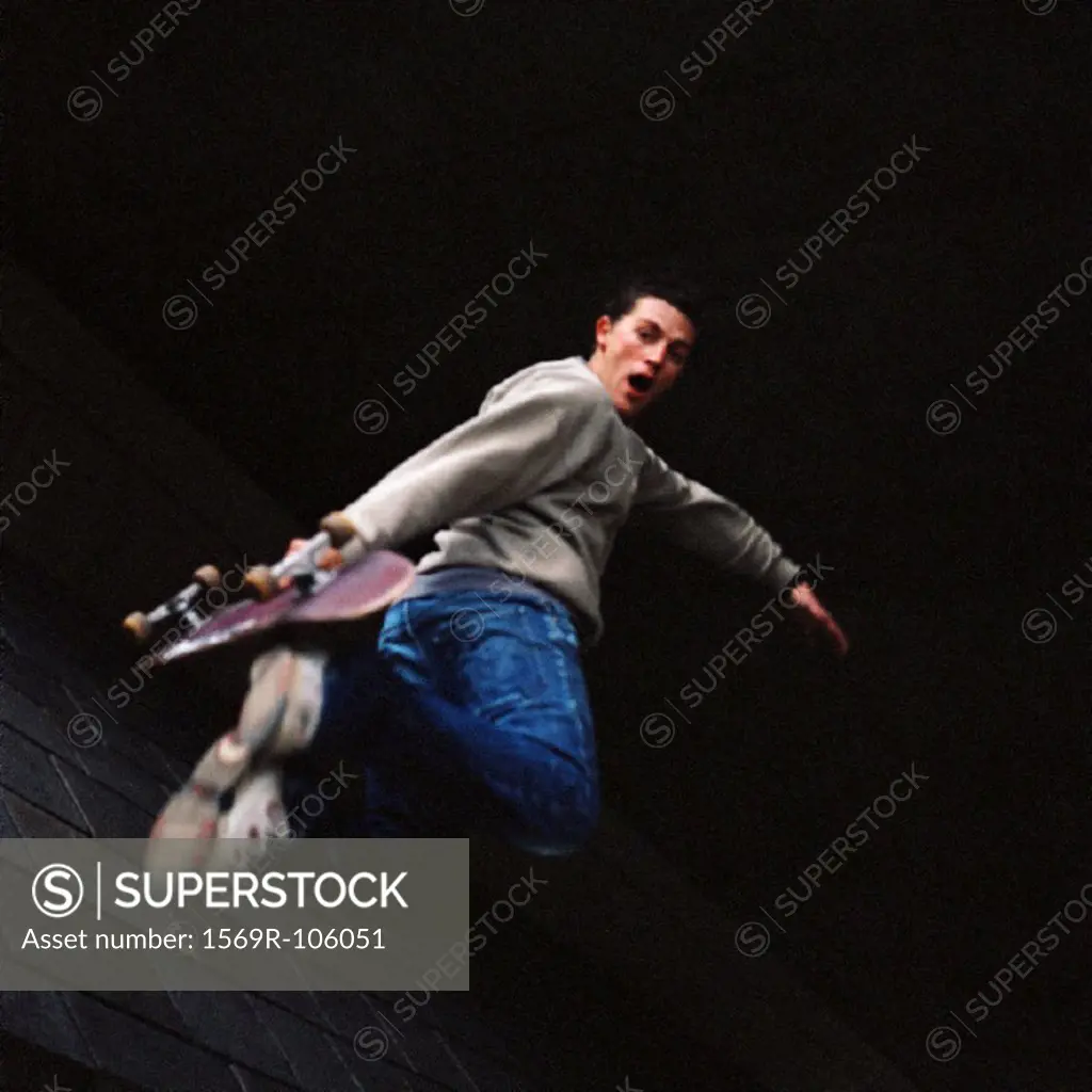 Young man in mid-air holding skateboard
