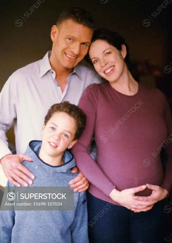 Pregnant woman and man standing with child, smiling, portrait