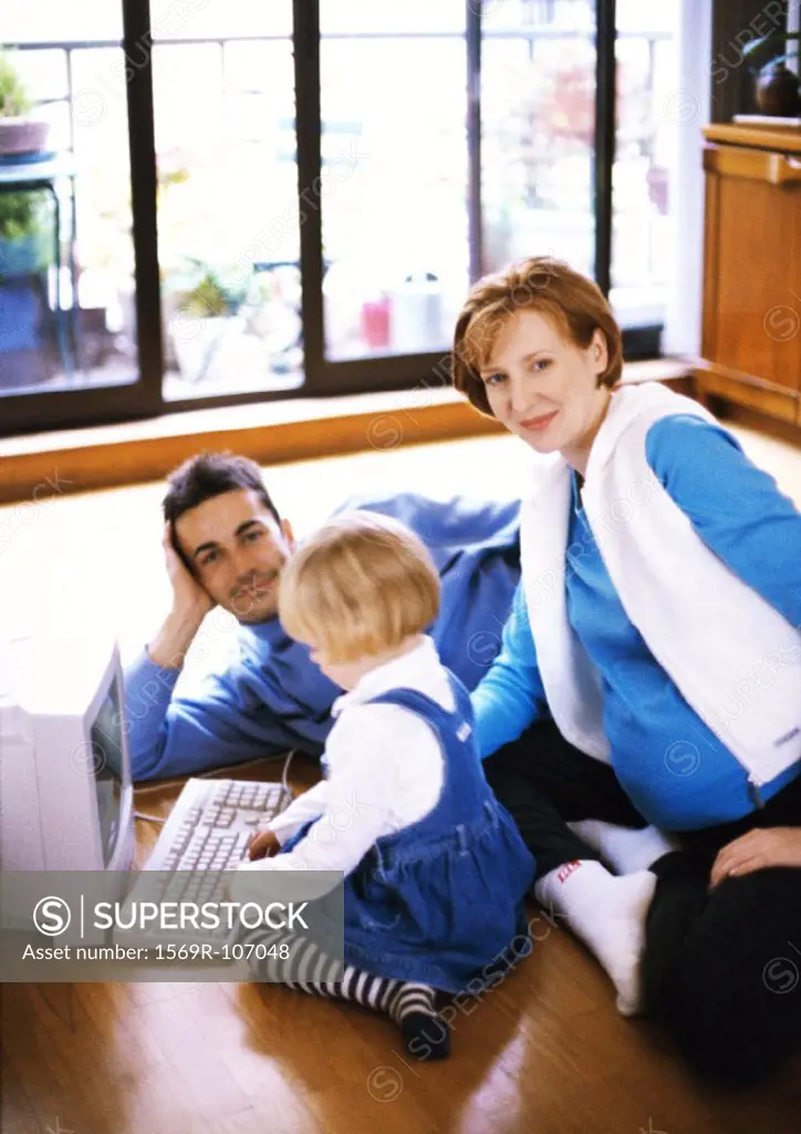 Pregnant woman and man on floor with child touching computer keyboard