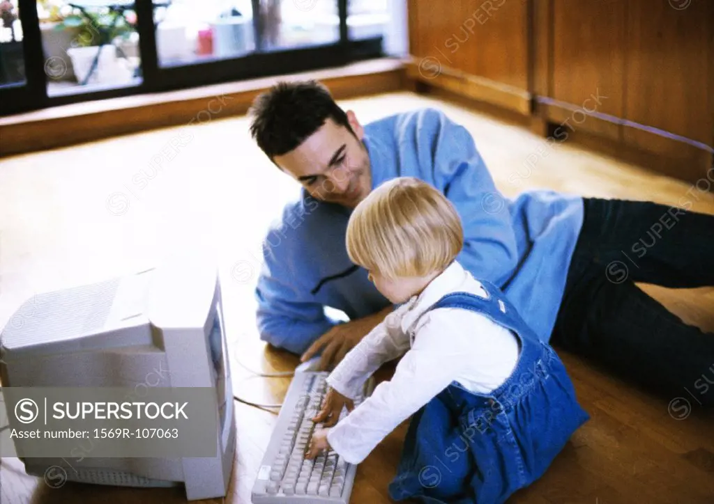 Man lying on floor, child in front of computer