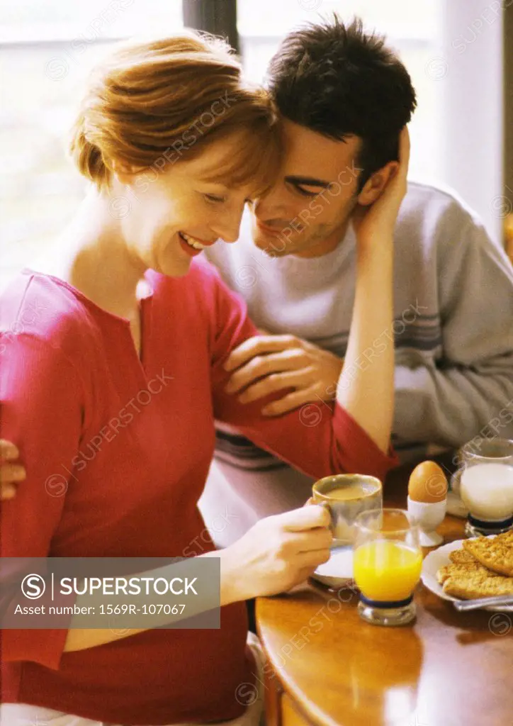 Pregnant woman and man having breakfast, smiling