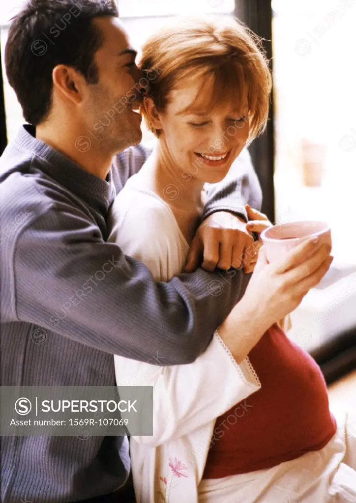 Man hugging pregnant woman from behind, smiling