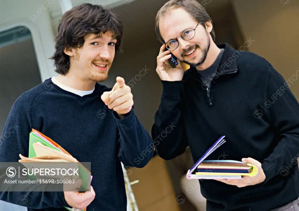 Two men looking into camera, one pointing, the other using cell phone, portrait