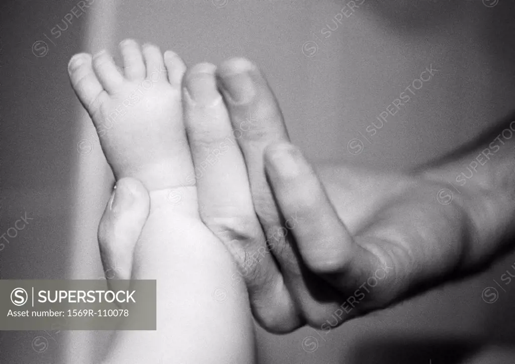 Adult hand holding baby´s foot, close-up, b&w