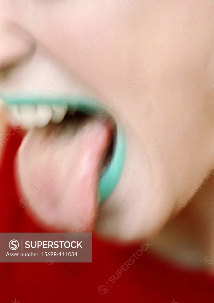 Tongue sticked out of mouth with green lipstick, close-up, blurred