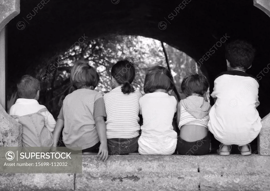 Children sitting under arch, viewed from the back, b&w