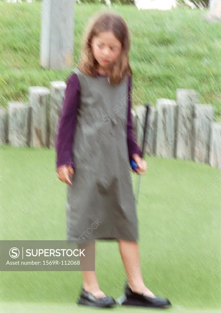 Girl standing on grass holding putter, blurred