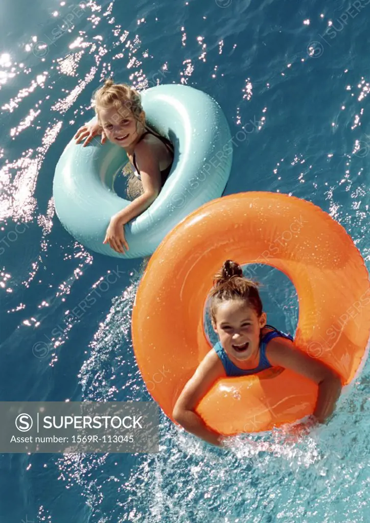 Two little girls floating in inflatable rings in water, high angle view