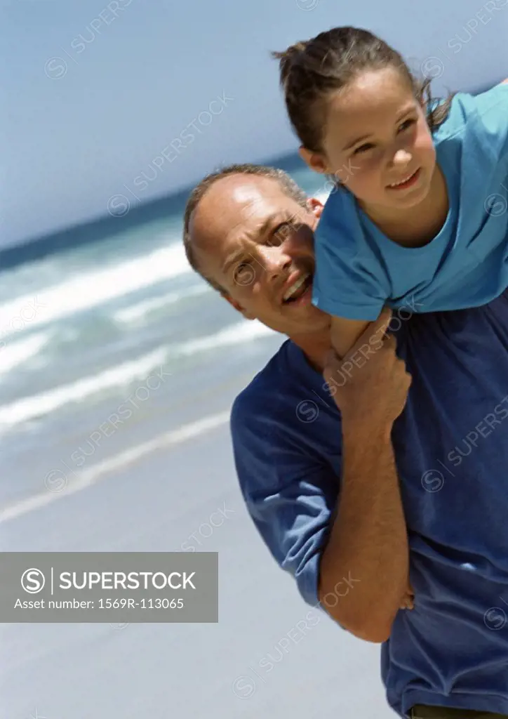 Man carrying young girl on shoulder on the beach