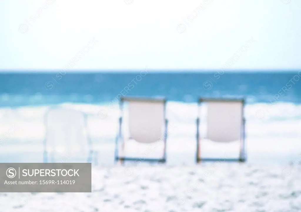 Three deckchairs lined up on beach, sea in background, blurred
