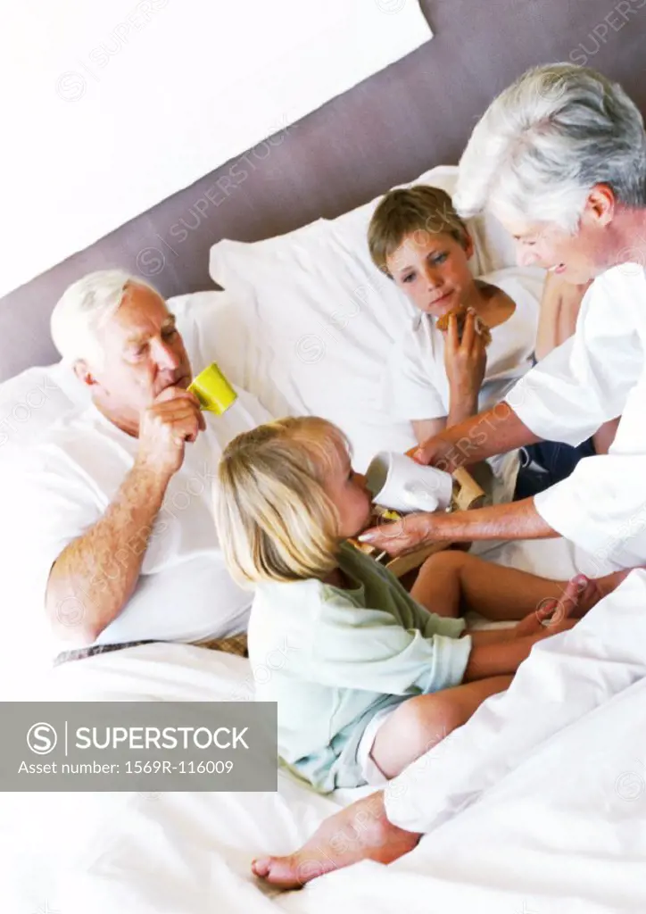 Grandparents and children on bed, drinking