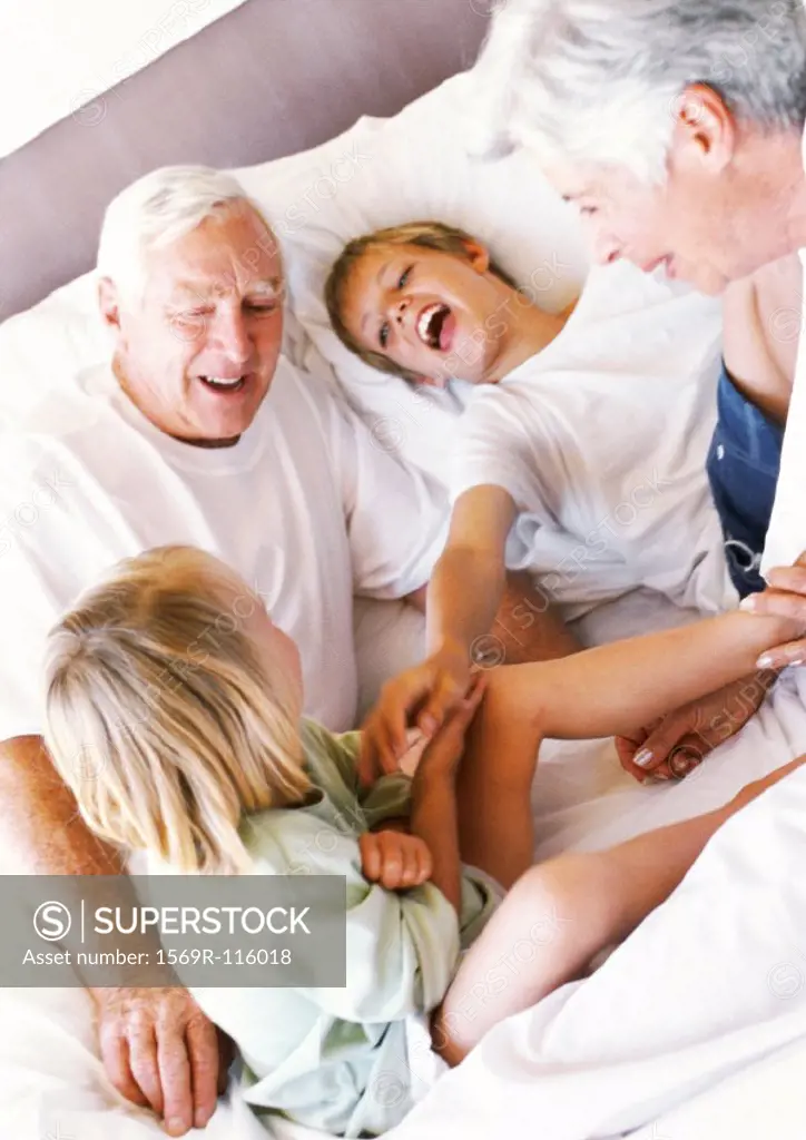 Grandparents and children sitting on bed, smiling