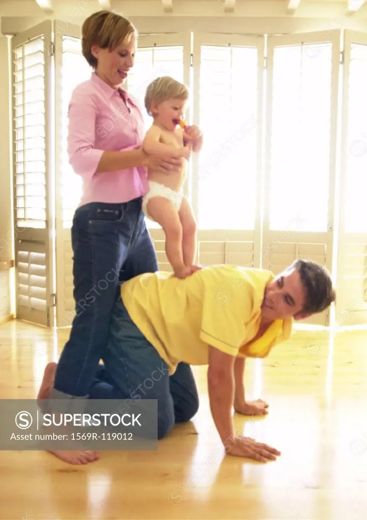Man on all fours, woman holding baby on his back