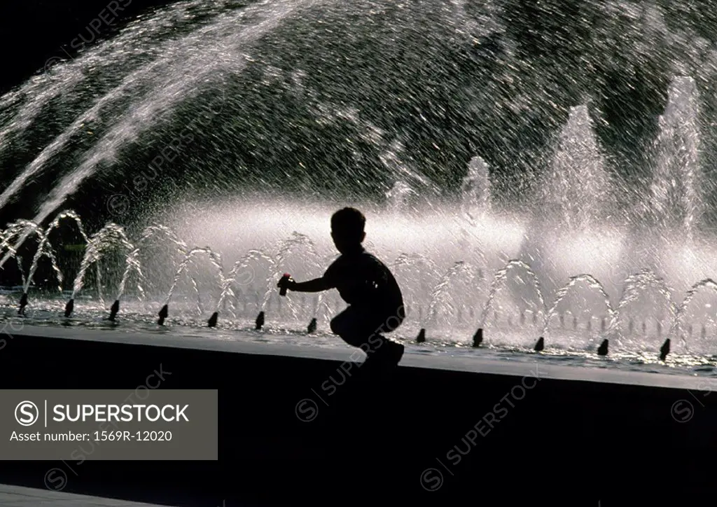 Silhouette of boy crouching on edge of fountain