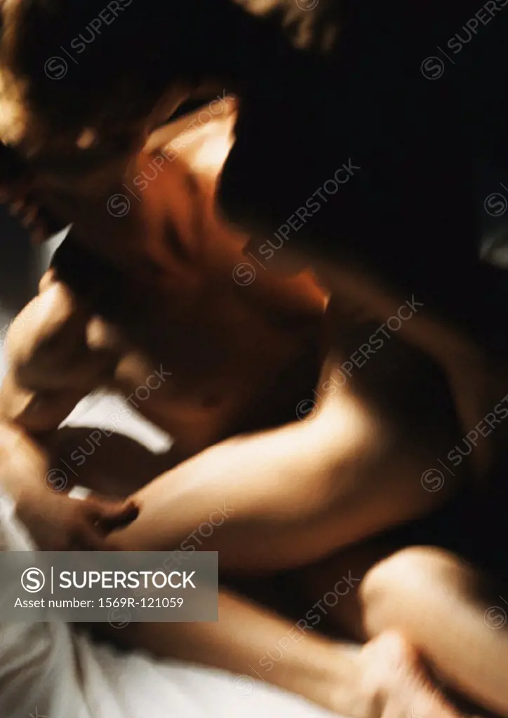 Nude couple making love, woman straddling man on bed, blurred