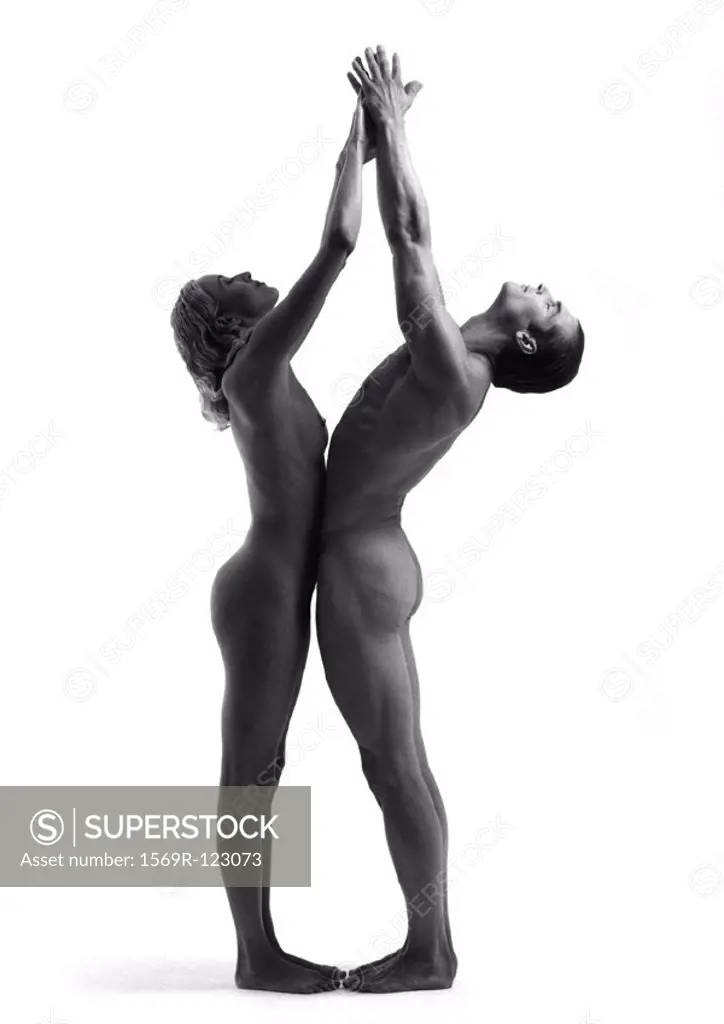 Nude man and woman standing toe to toe with heads back, hands together in air, b&w