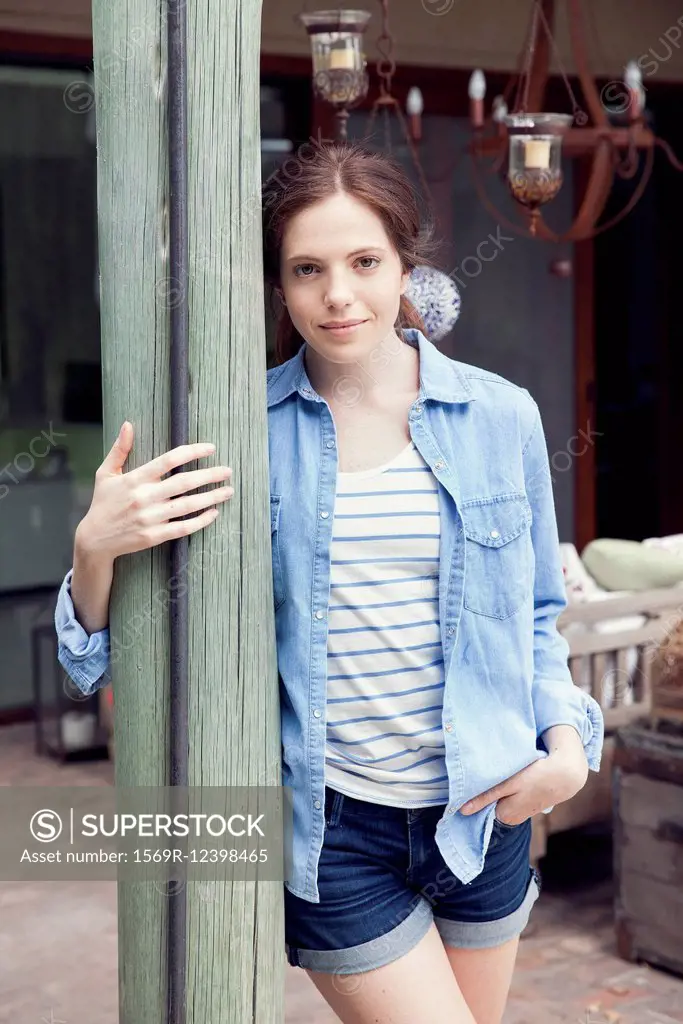 Young woman leaning against wooden post, portrait